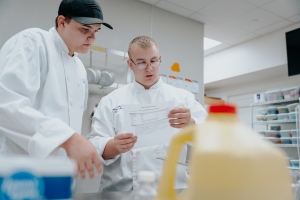 Two students in culinary attire making food.