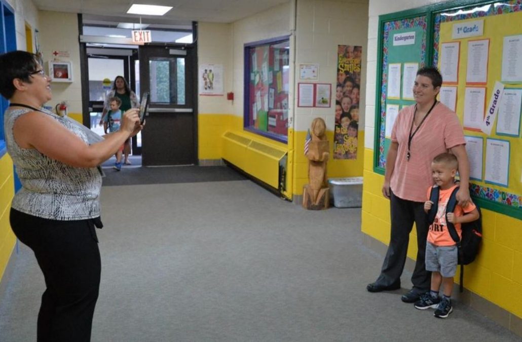 An adult taking a picture of another adult and child in hallway
