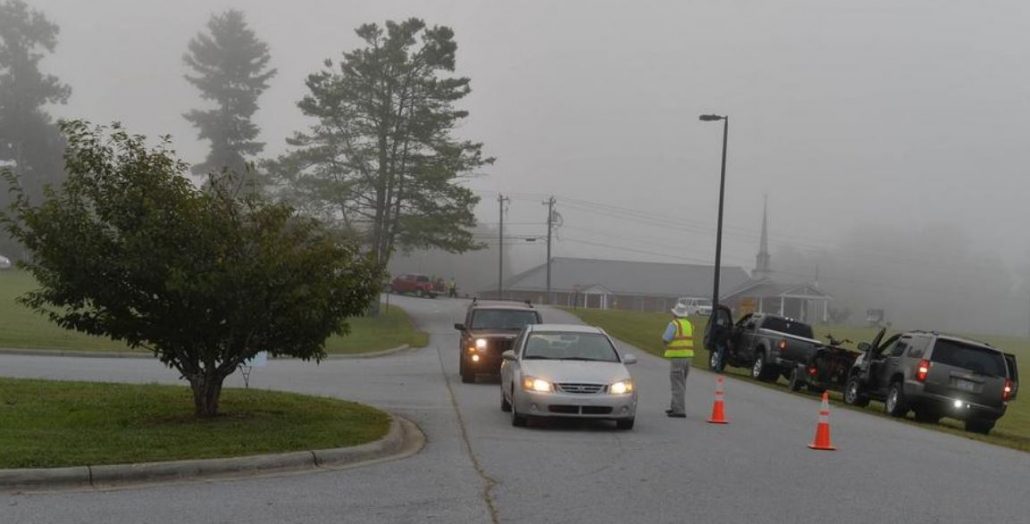 A person in bright safety vests directing traffic into school