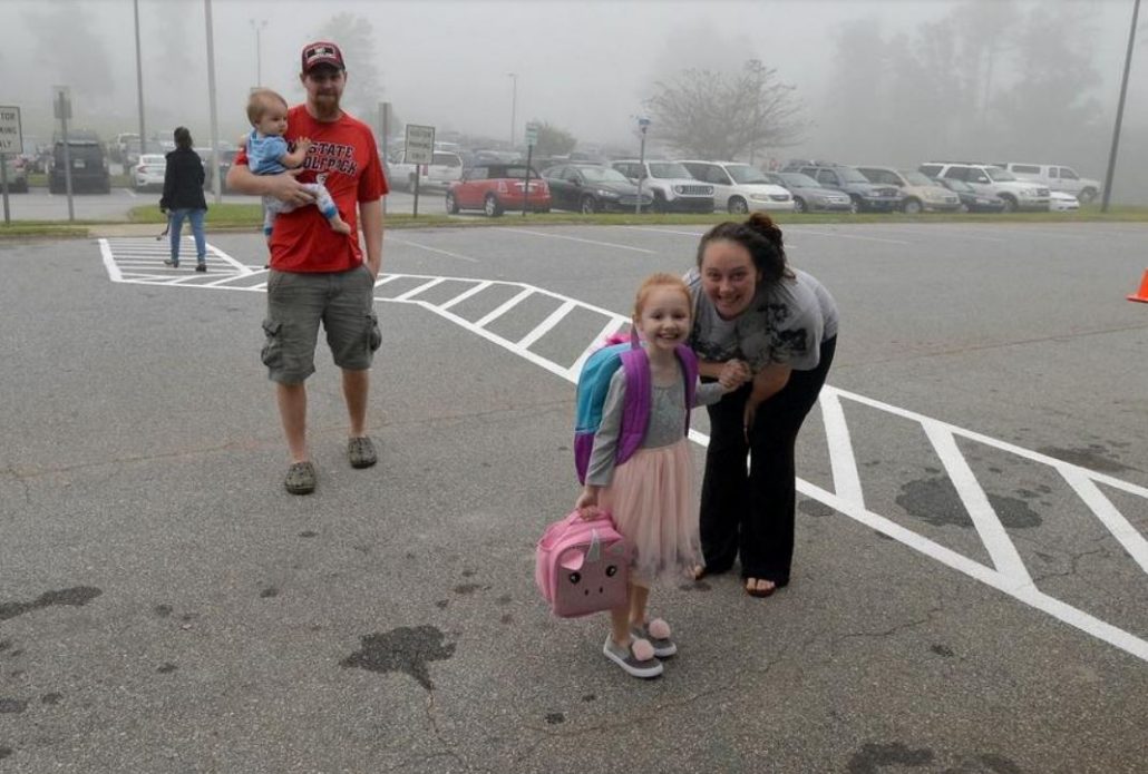 A father holds a baby while the mother poses with new student in crosswalk
