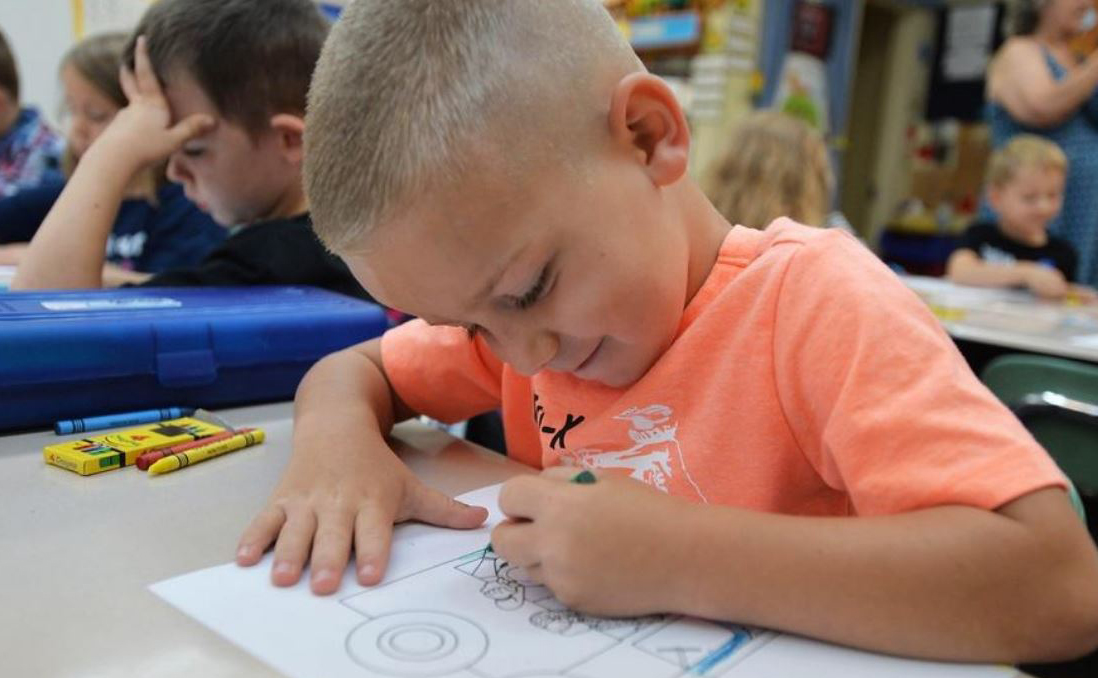 A young boy in orange shirt writes on paper