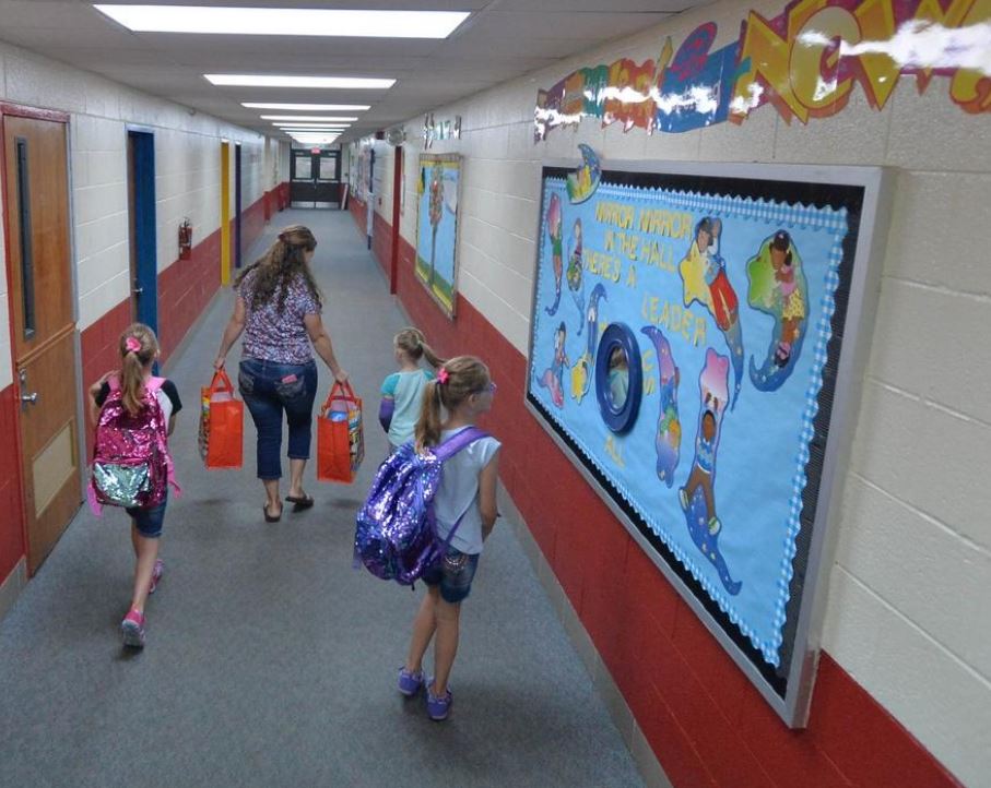 3 students and an adult walking down school hallway. One student stops to look at art on the wall
