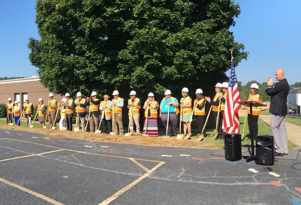 People in hard hats and safety vests holding shovels. 