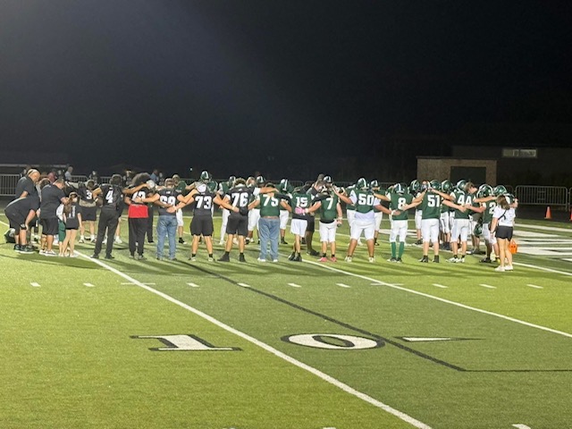 football team arm in arm in a huddle on the field
