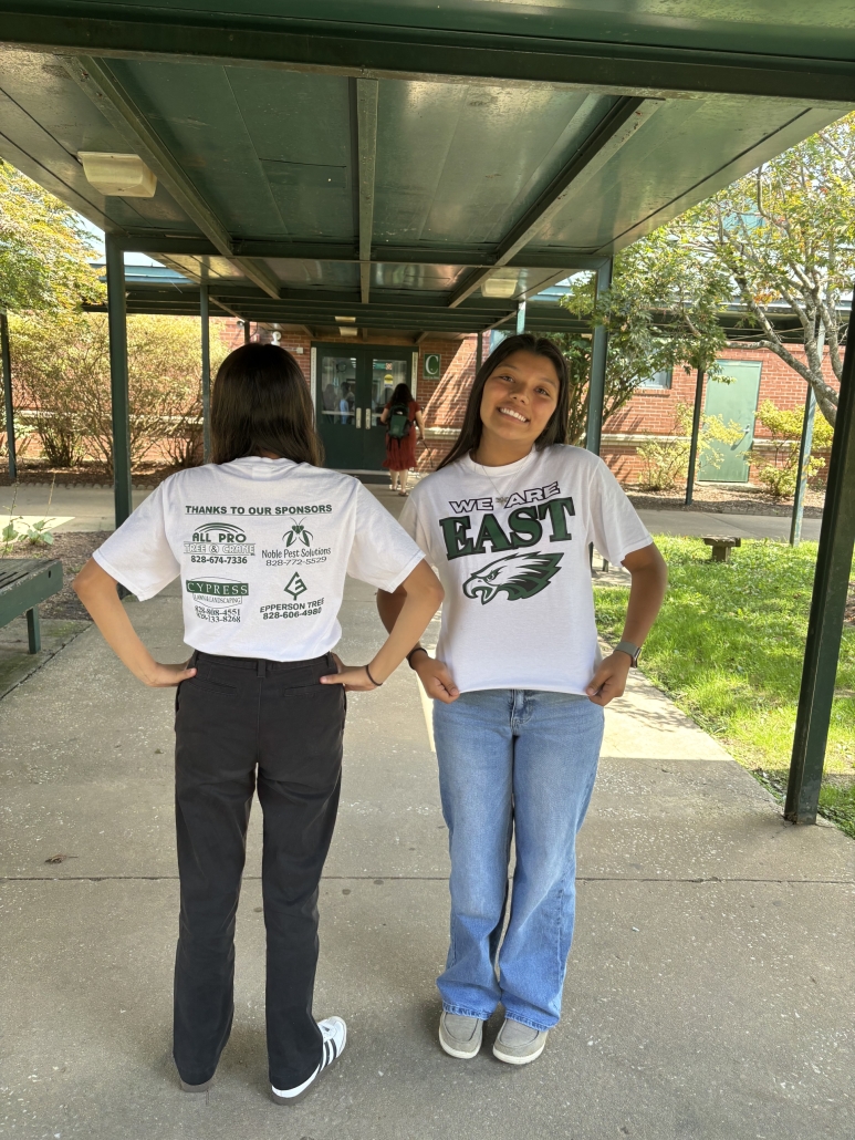 one student showing back and one student showing front of We Are East shirts in breezeway