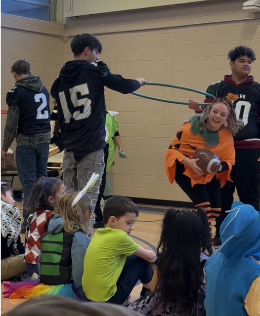 Football players playing a hula hoop game with Ms. Coggins