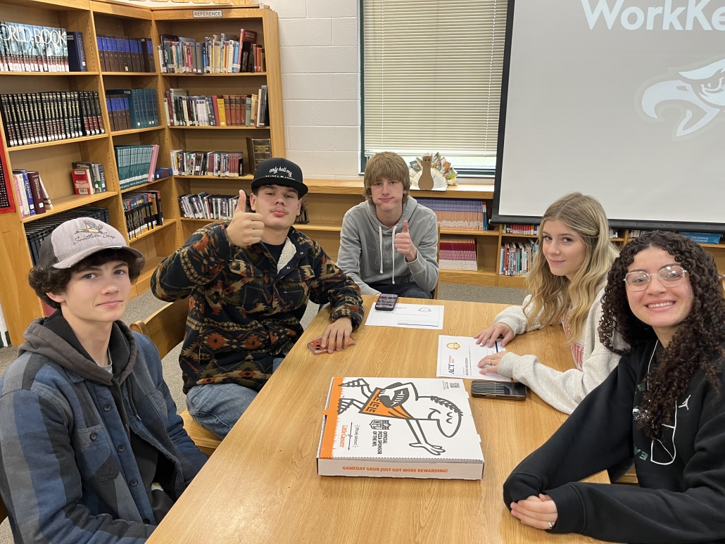students at a table with pizza box enjoying the celebration