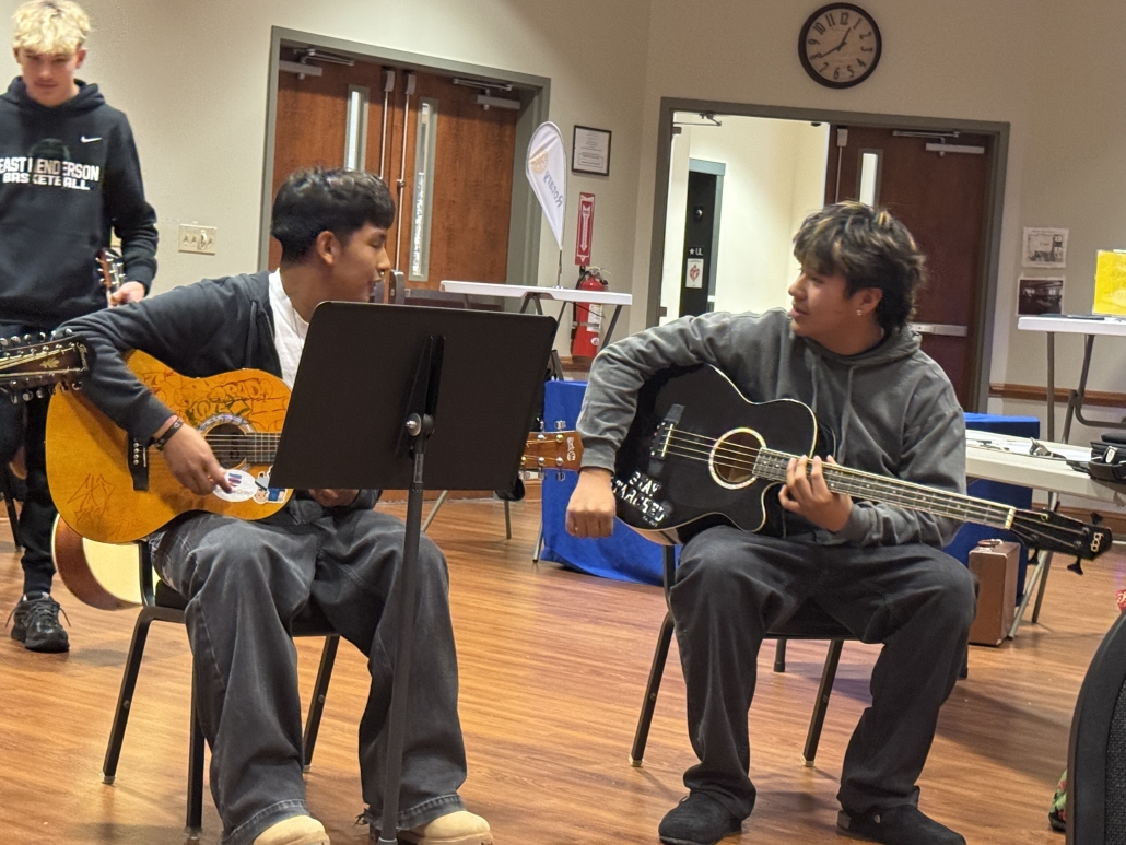 Two students looking at each other while playing guitar