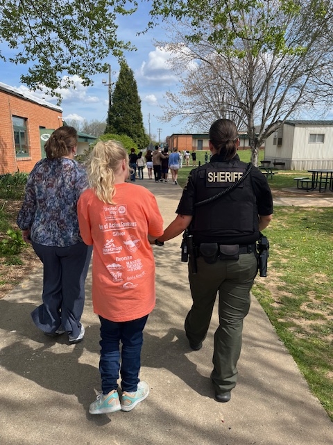 Ms. Theresa and Deputy Maybin walking Ellie to the egg hunt