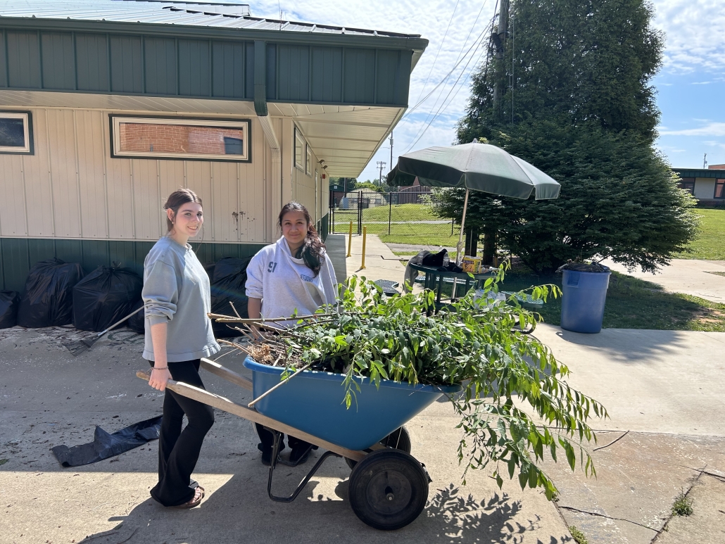 Students moving wheelbarrow with brush