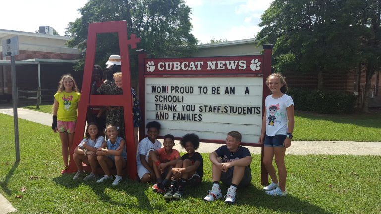 Students standing in front of school marquee sign.