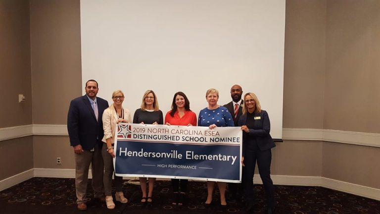 Adults standing around Distinguished School Nominee Banner