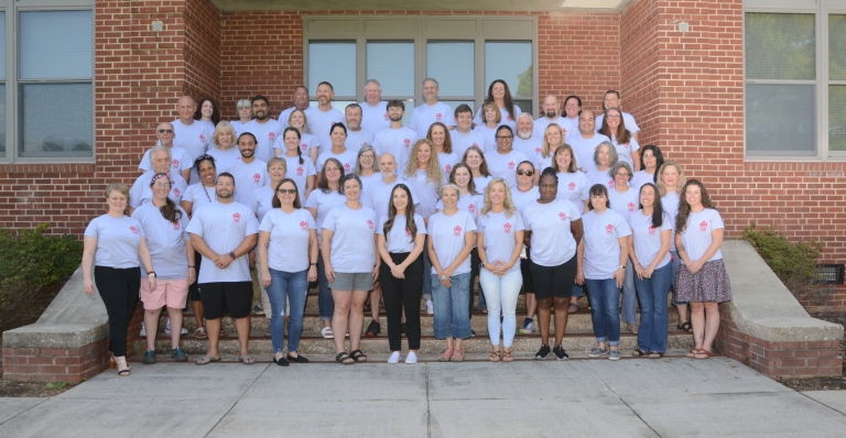 Photo of HMS faculty and staff standing on steps of the brick school building, smiling.