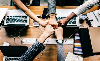 5 team members fist-bumping over computers to show positive collaboration