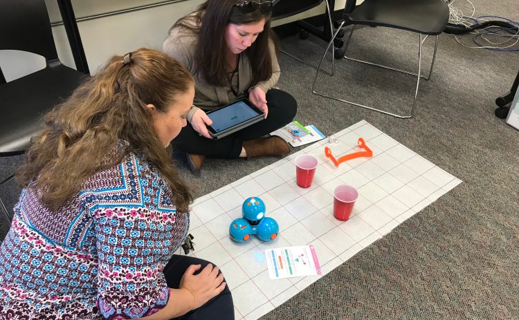 Two teachers working with Dash using cups, a grid mat, and an iPad