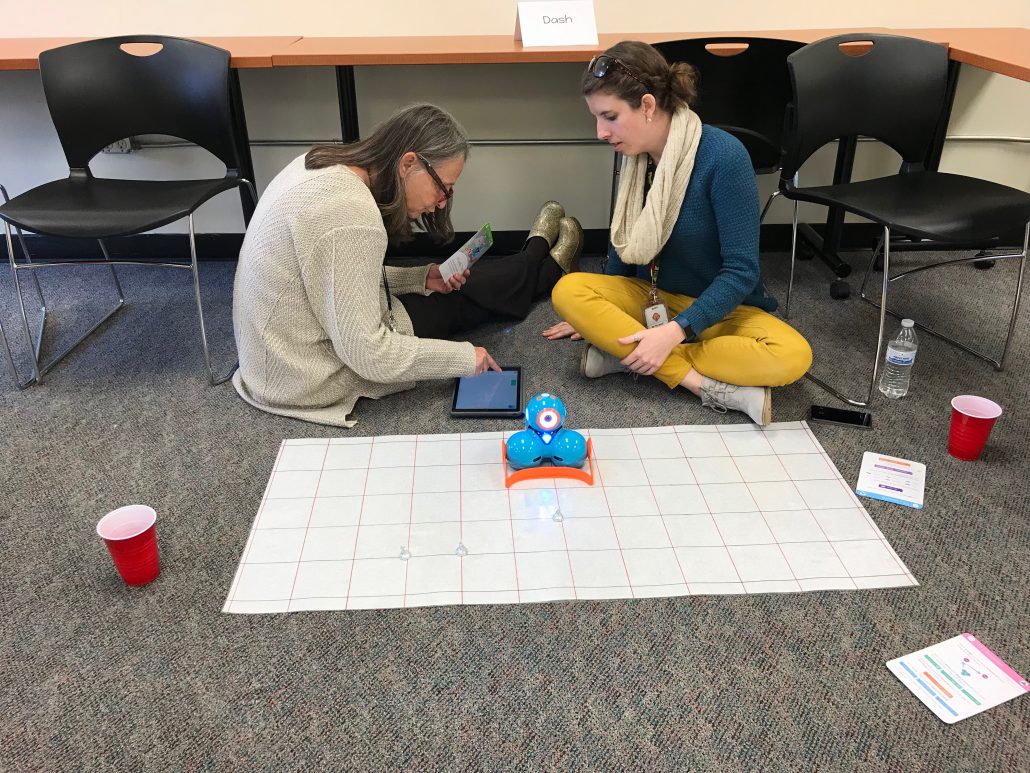 Two teachers working with an iPad and Dash wearing the bulldozer attachment