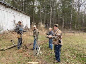 4 men work on fixing barbed wire fence.