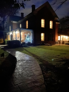 Farmhouse at night. Lights are on at the porch and in the windows.