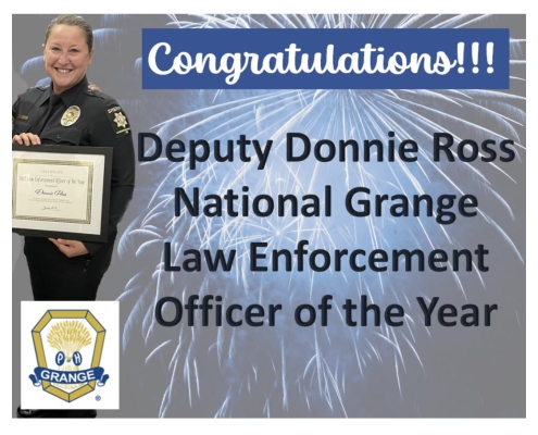 Fireworks on gray background with sheriff deputy woman in black uniform holding a framed certificate. Congratulations!!! Deputy Donnie Ross National Grange Law Enforcement Officer of the Year. Grange symbol.