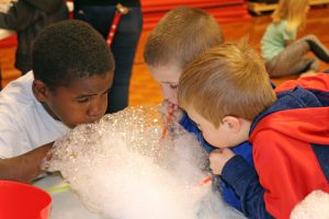 Three students blow bubbles in a tub.