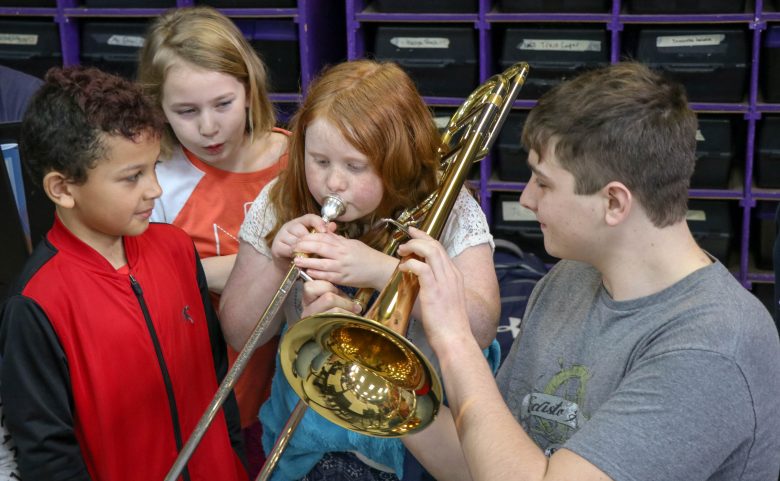 high school student holds trombone for elementary student to play