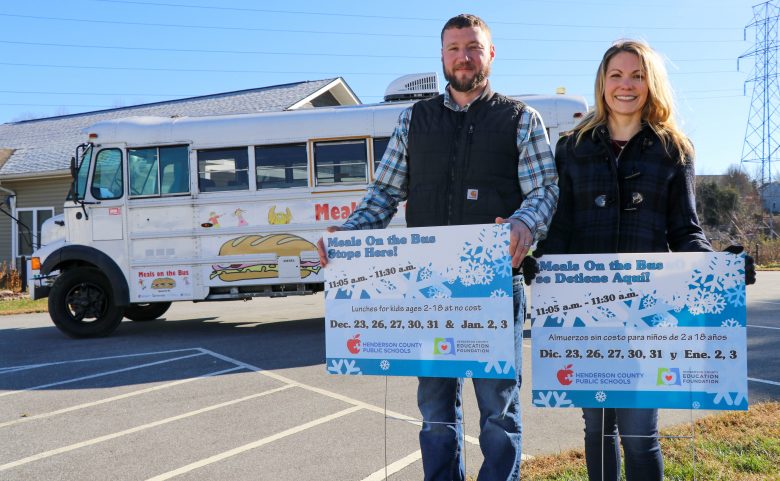 2 people standing outside with signs and bus