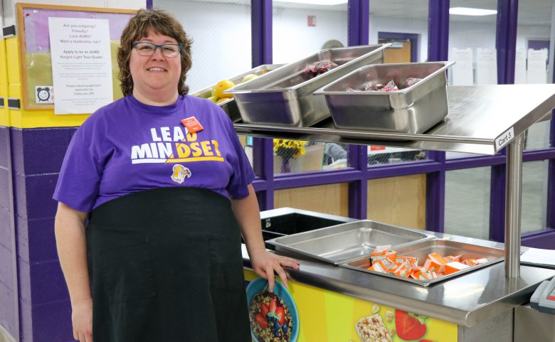 woman in apron standing in front of food cart