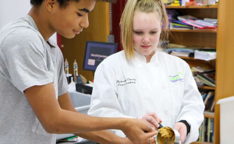 two students adding ingredients to pot