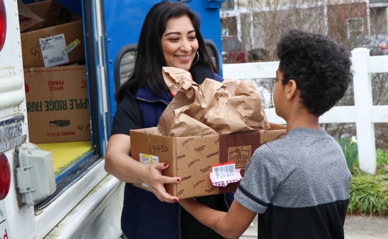 woman handing box of food to child
