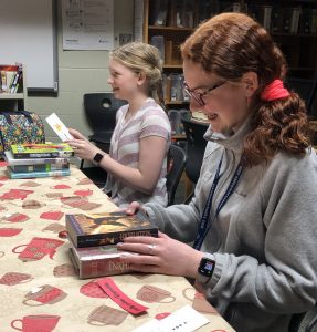 two middle school girls smiling as they look through books