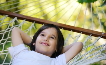 A young child laying in a hammock looking up and smiling