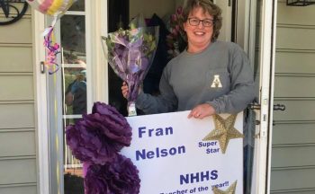 teacher holding balloons and sign outside house