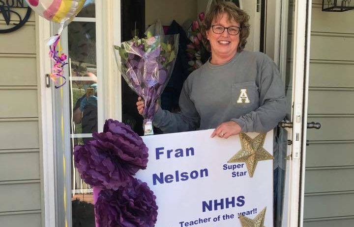 teacher holding balloons and sign outside house