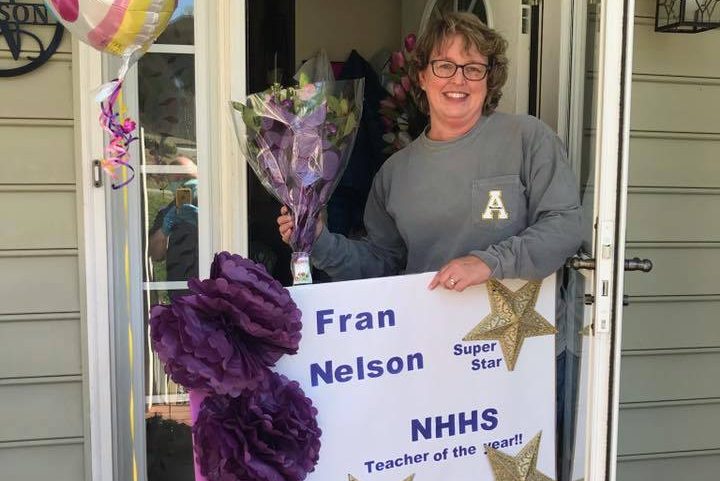 teacher holding balloons and sign outside house