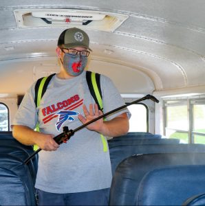 custodian using backpack sprayer on bus