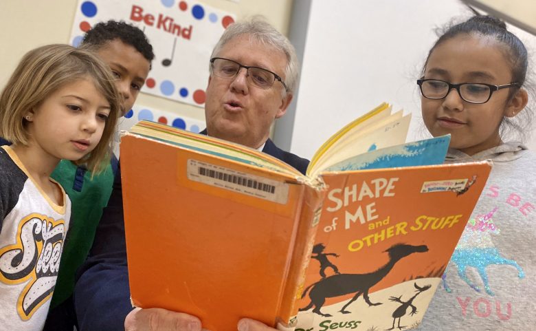 superintendent reading Dr. Seuss book to 3 elementary students