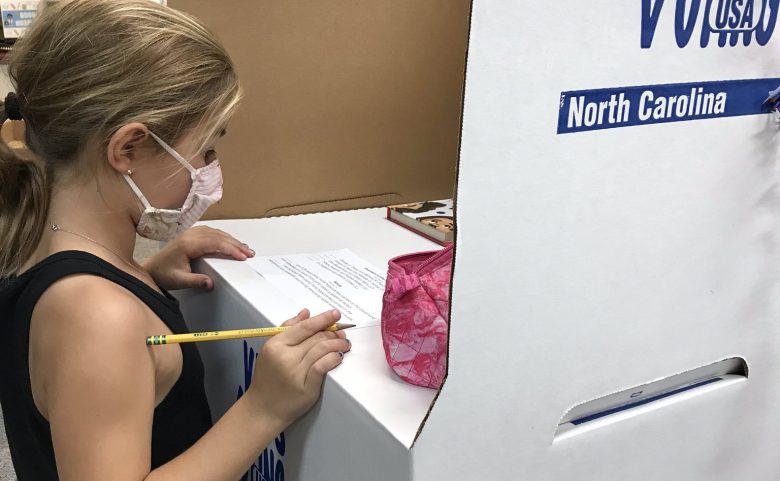 elementary-age girl wearing mask at a voting booth