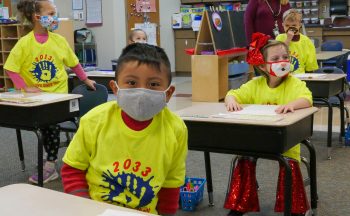 four kindergarteners at desks in neon shirts