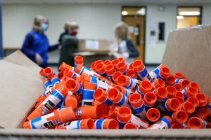 box full of glue sticks with 3 children in background