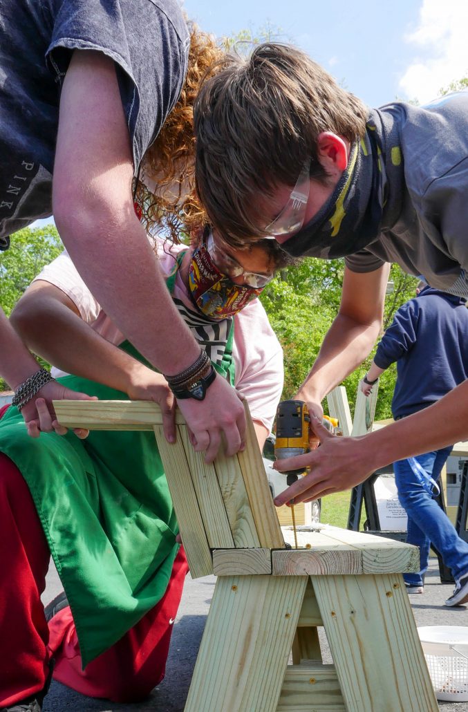 three students lean over bench to drill a screw