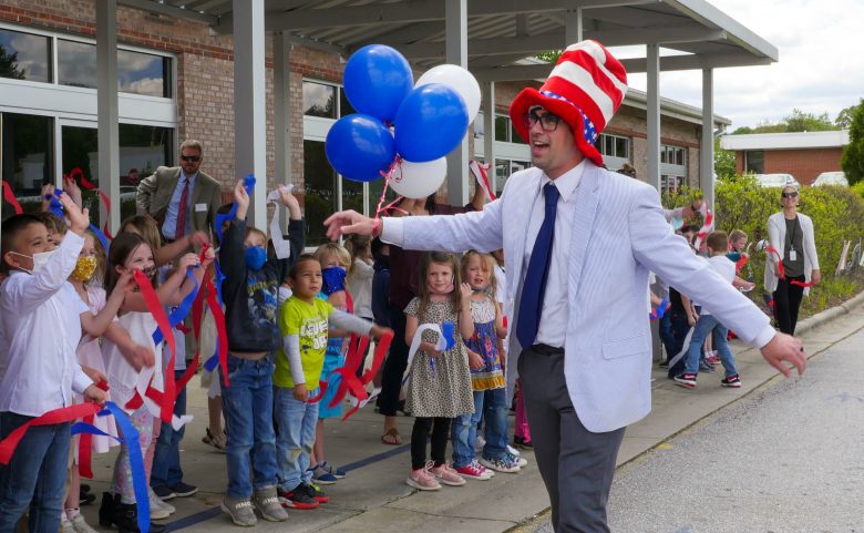 man in tall striped hat and balloons being cheered by students