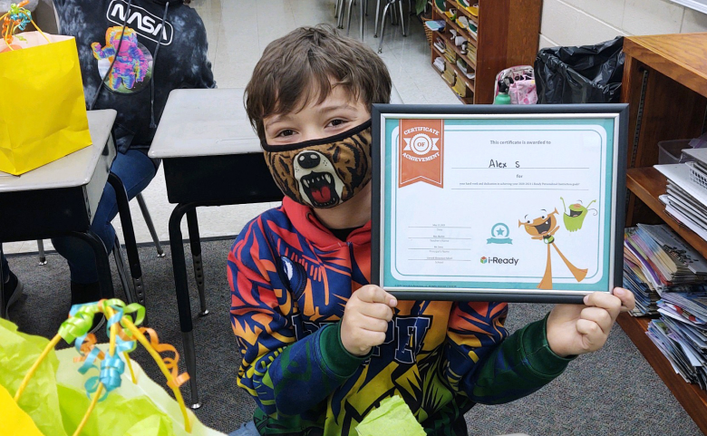 student in face mask smiling, holding up certificate