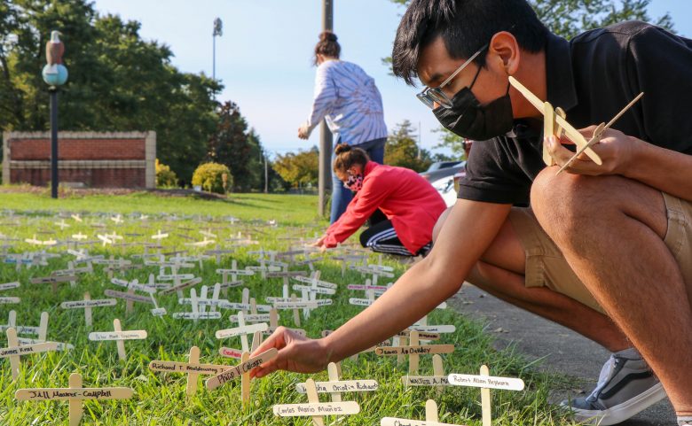 student placing small wooden crosses in grass
