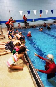 students lined up along edge of pool while instructor gives lessons