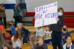 student holding up sign in auditorium that reads "Congratulations Mr. Mitchell"