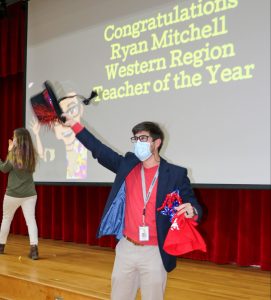 teacher waving tophat in the air, in front of sign that reads "Congratulations Ryan Mitchell Western Region Teacher of the Year"