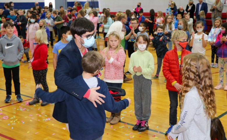 teacher accepting hugs from long line of students in auditorium