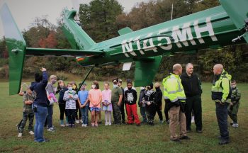 students gathered outside under the tail of a helicopter