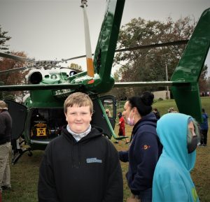 student outside, smiling, with helicopter behind