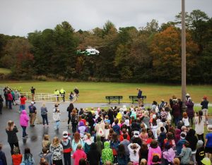 helicopter landing in field as schoolchildren stand and watch